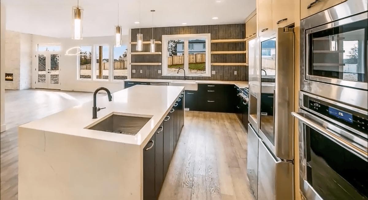 Modern kitchen with large island, dark cabinets, stainless steel appliances, and open access to a living area with a fireplace.
