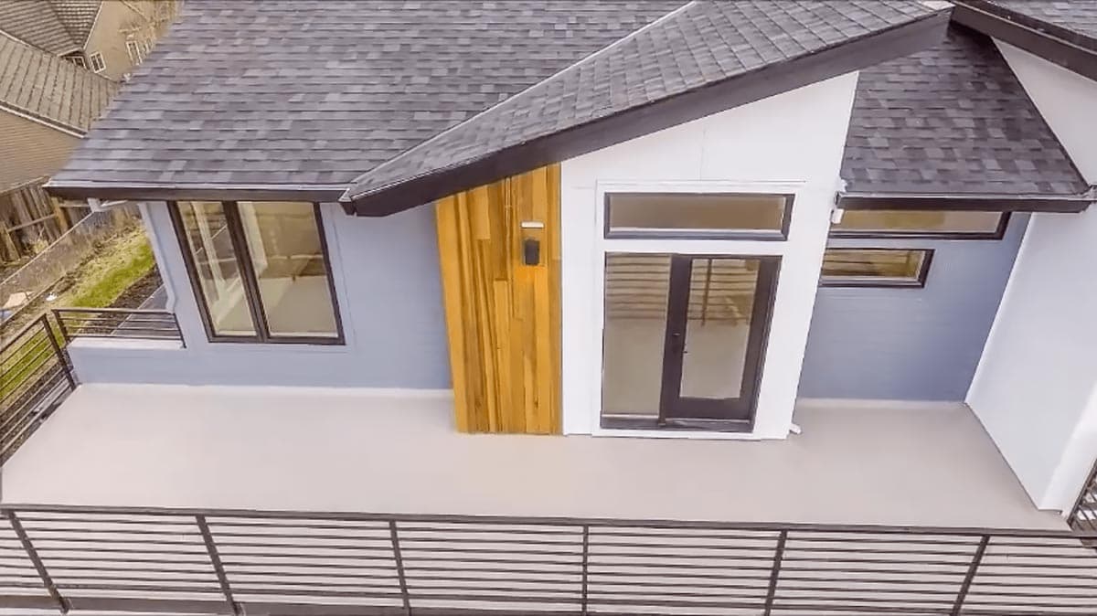 Modern house plan exterior with dark-trimmed windows, wood accent, and metal railing on a deck.