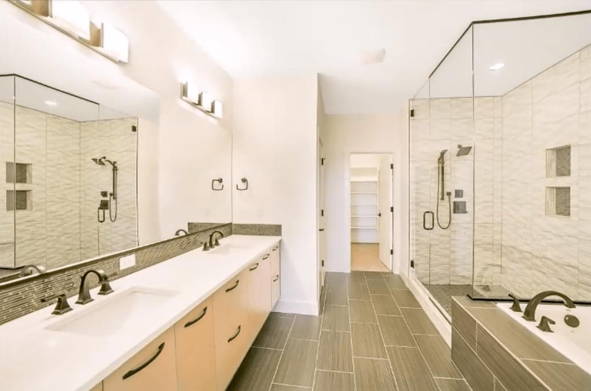 Bathroom features double vanity, walk-in shower with tiled walls, and a soaking tub. Leads to a closet with shelving.