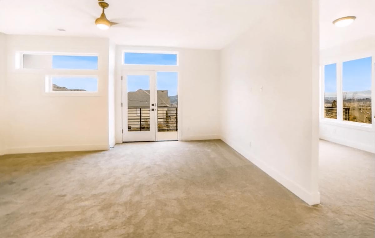 Interior view of an empty room with a ceiling fan, horizontal windows, and double doors opening to a balcony.