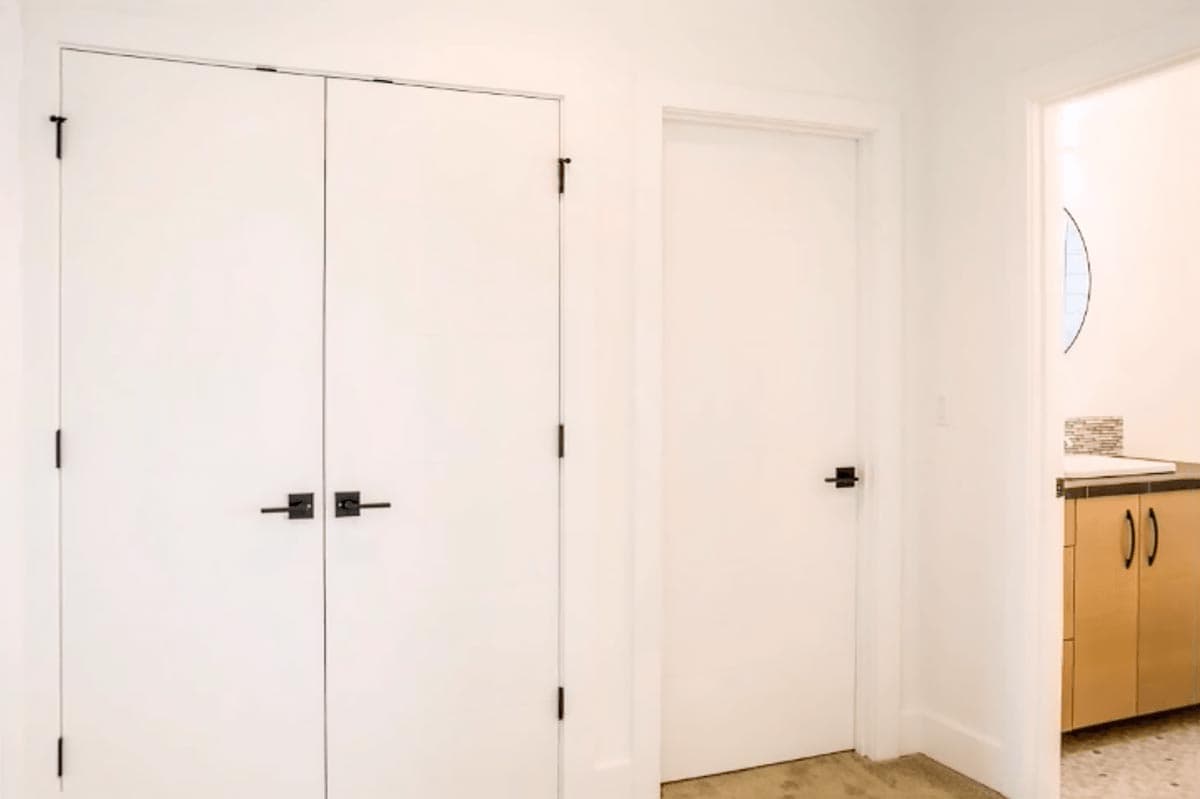 Interior view of two white doors with black hardware and a cabinet with two doors visible through an opening.
