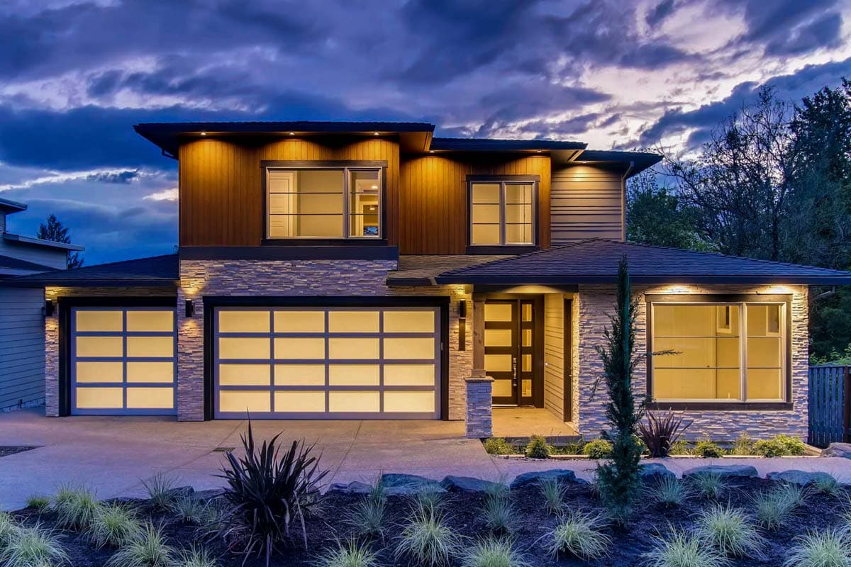 Modern house plan exterior with stacked stone, wood siding, two glass garage doors, and geometric entry.