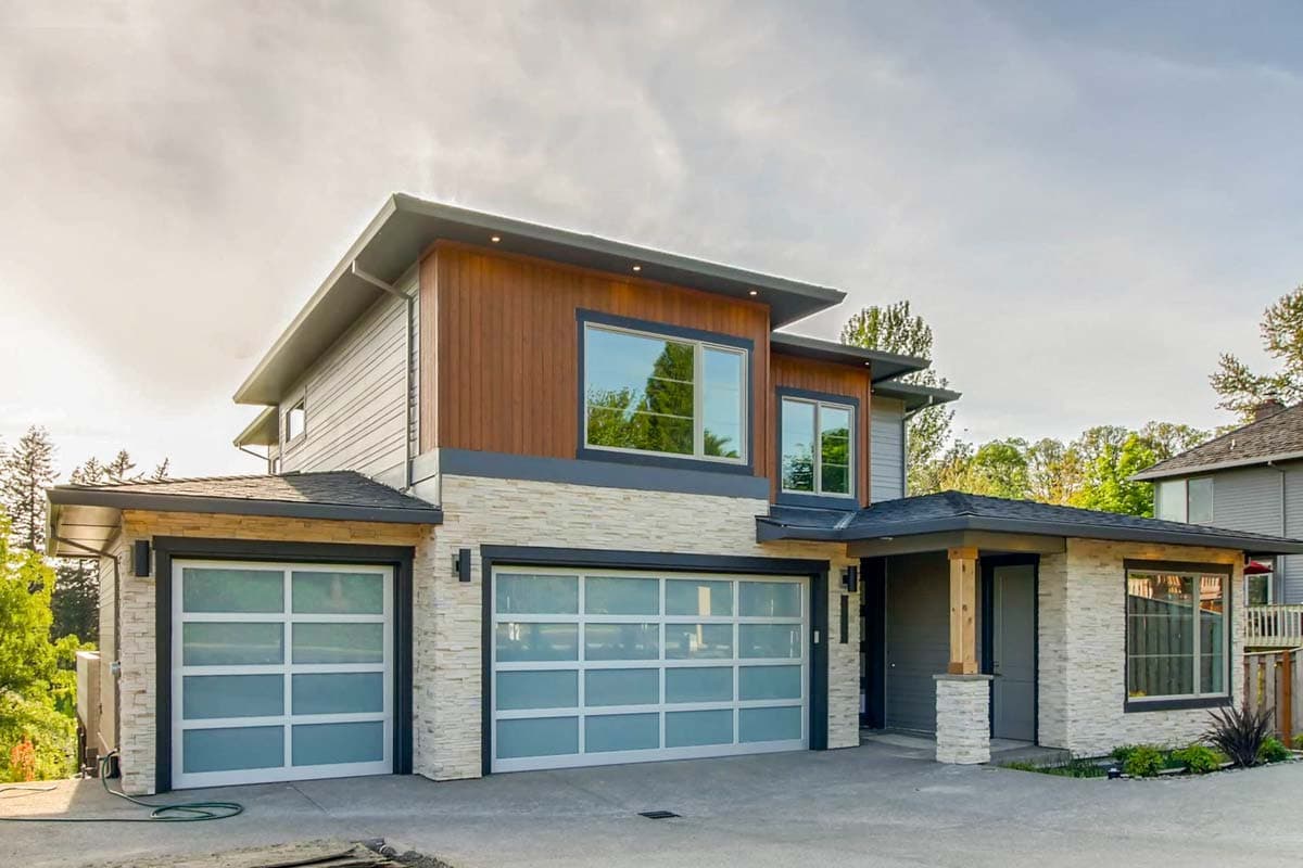 Modern house plan exterior with stacked stone, wood siding, and frosted glass garage doors. Two stories with flat rooflines.