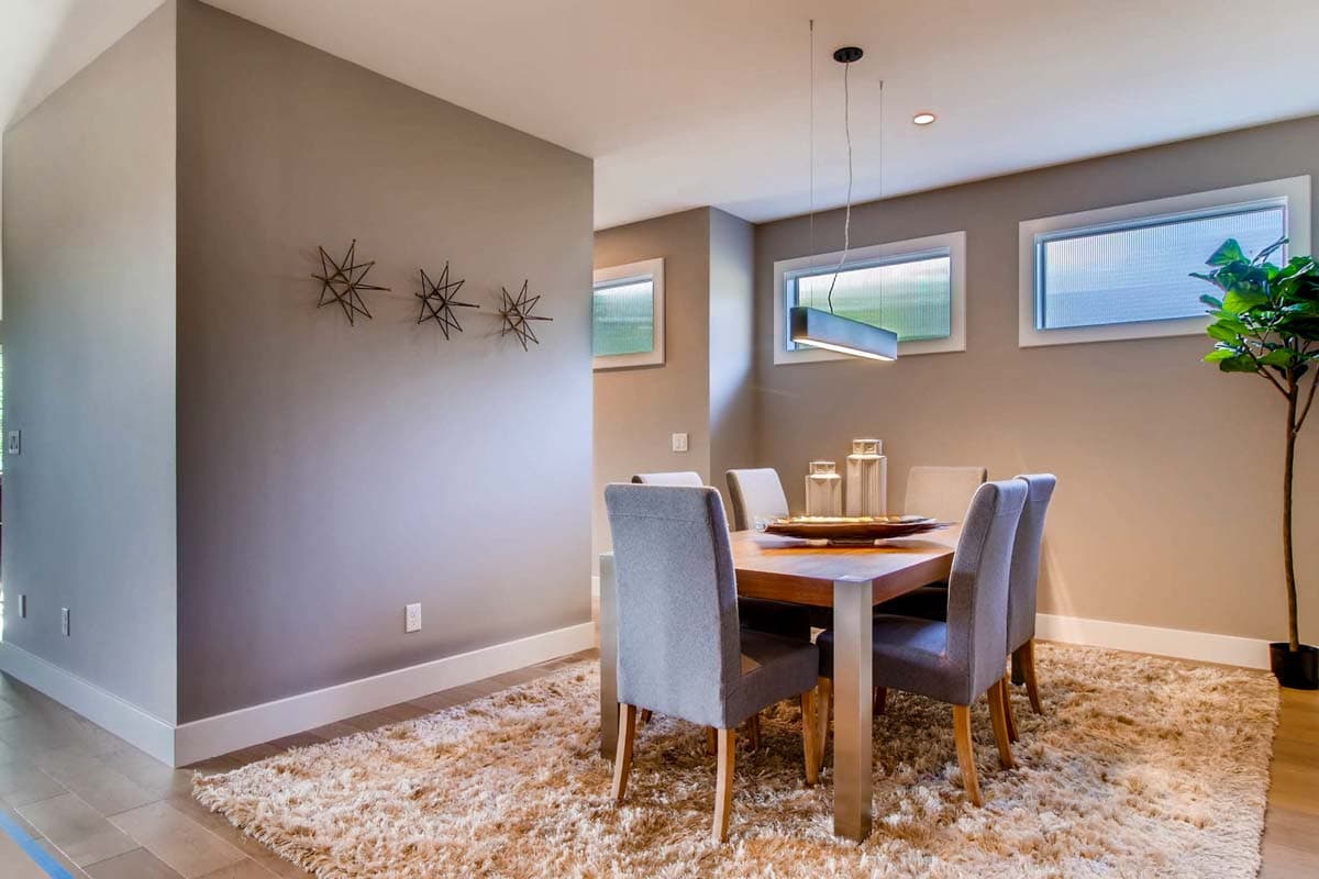 Interior dining room with a wood table, upholstered chairs, linear pendant light, and three horizontal windows.