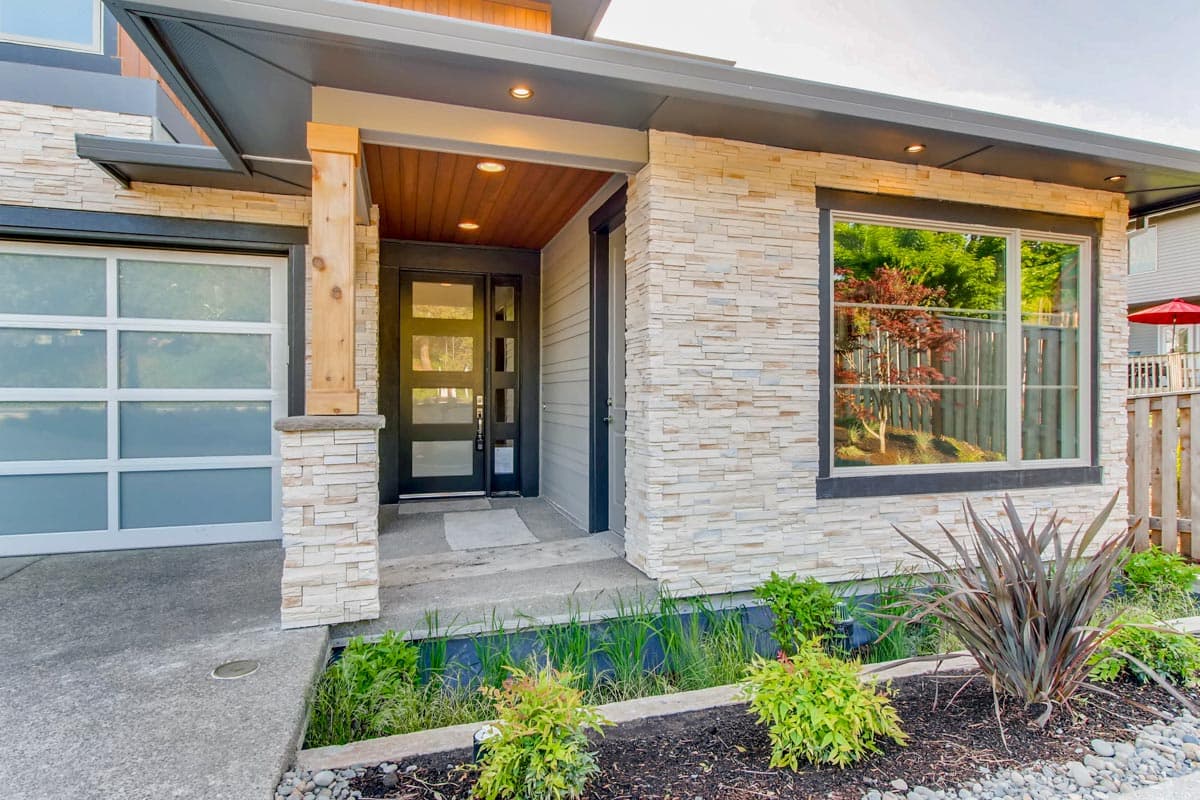 Modern house plan exterior with stone facade, glass garage door, wood-accented entry, and multi-pane glass door.