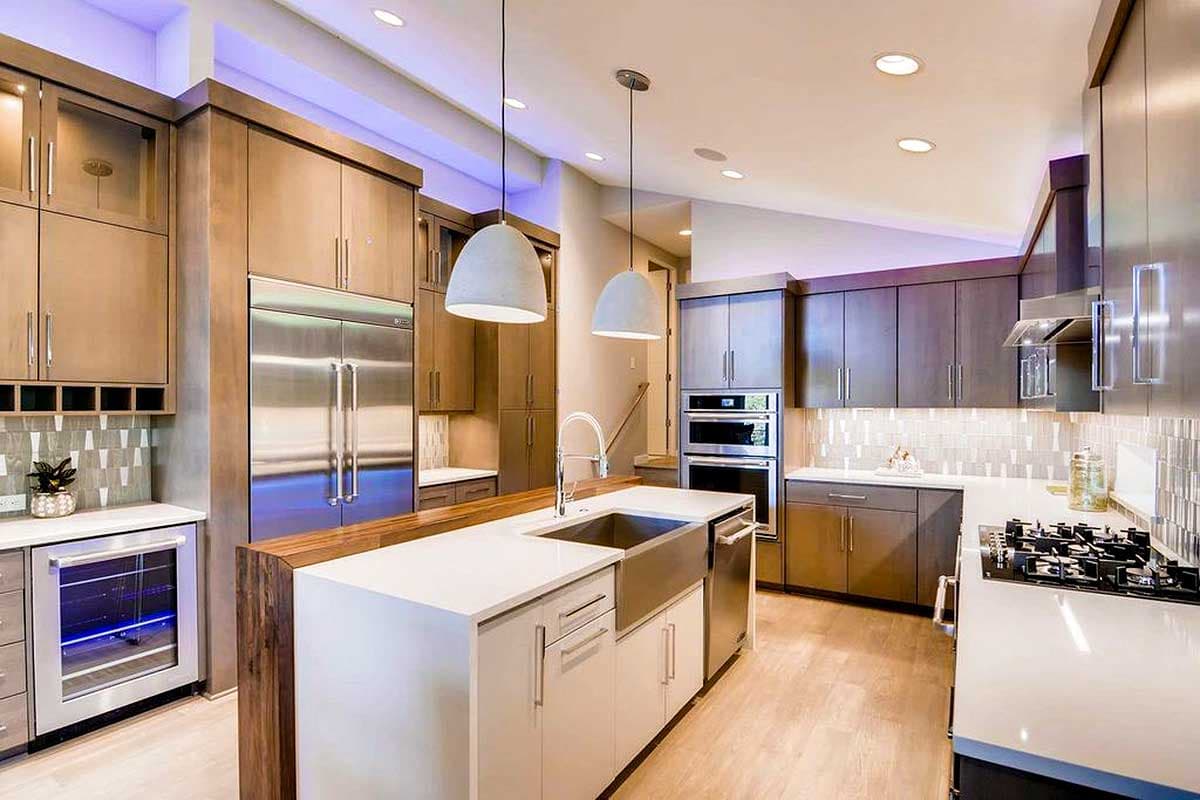 Modern kitchen with wood cabinetry, stainless steel appliances, large island with sink, and pendant lighting.