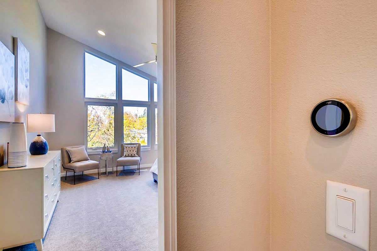 Bedroom with vaulted ceiling, large angled window, dresser, and thermostat control on wall.