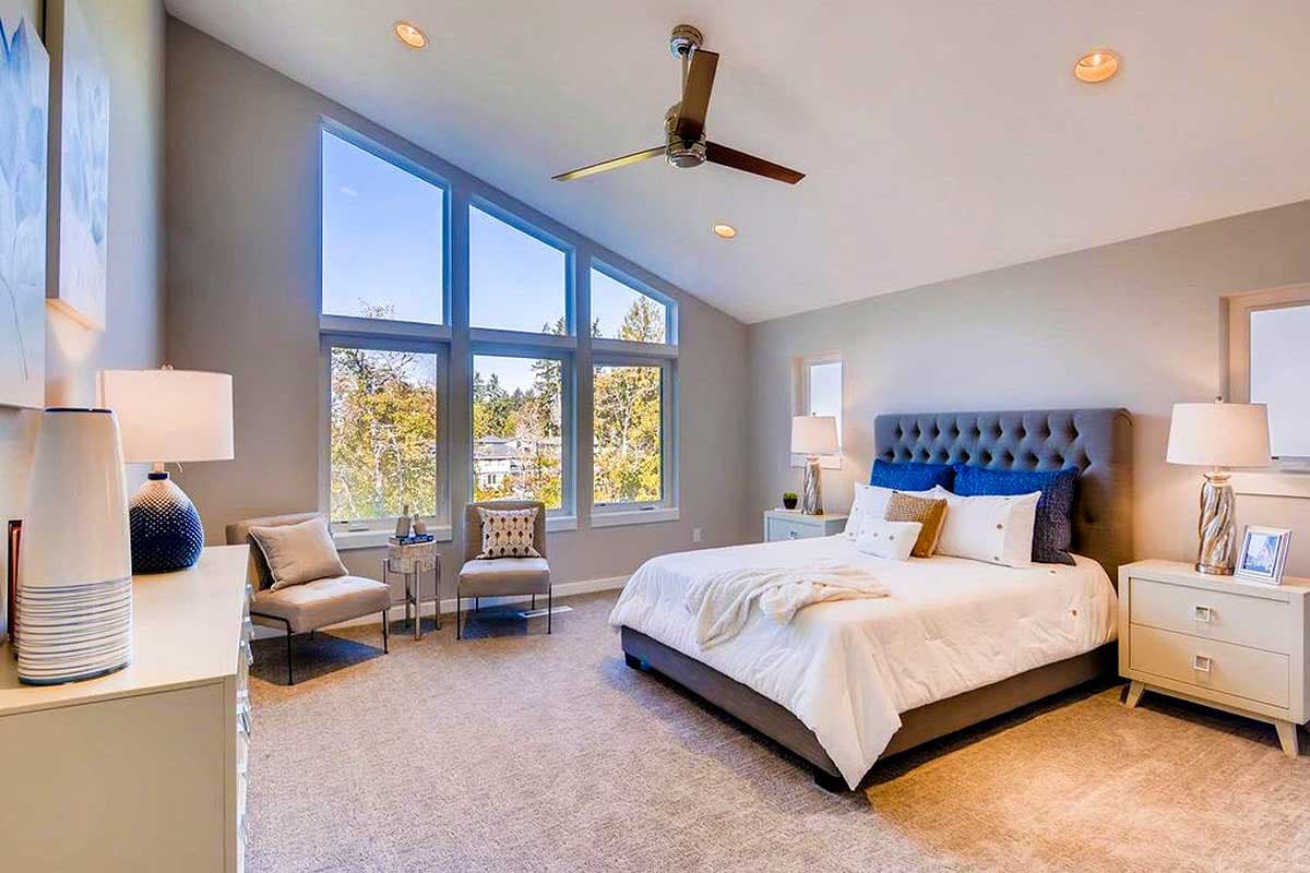 Modern bedroom with vaulted ceiling and large, angled windows offering natural light and treetop views.