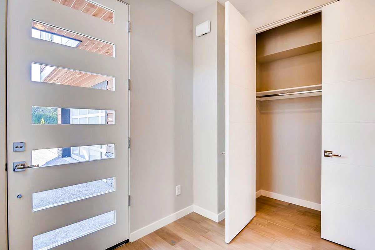 Modern front door with horizontal glass panels opens to interior with closet.