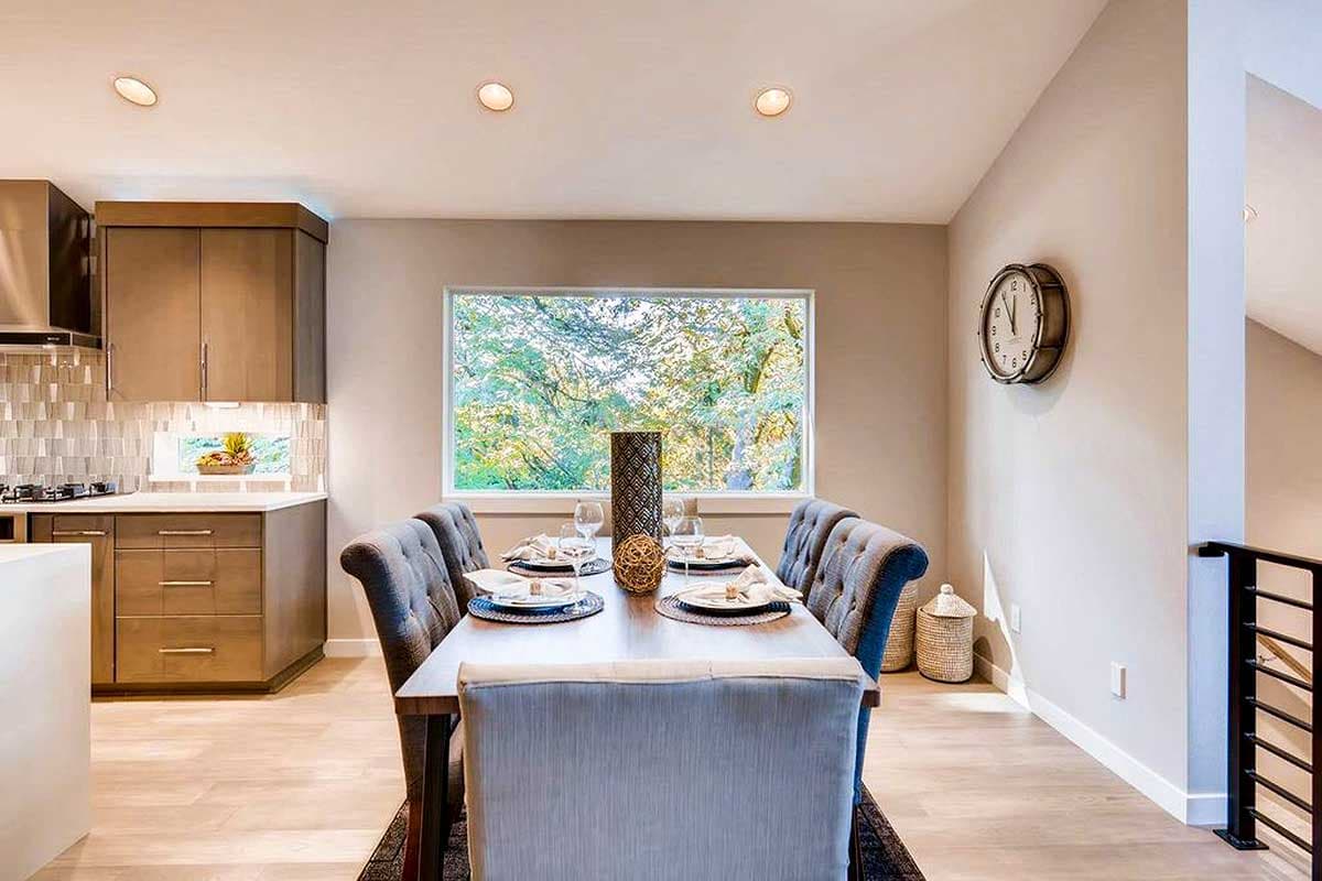 Dining room with tufted chairs, large window view, and adjacent kitchen with modern cabinetry.