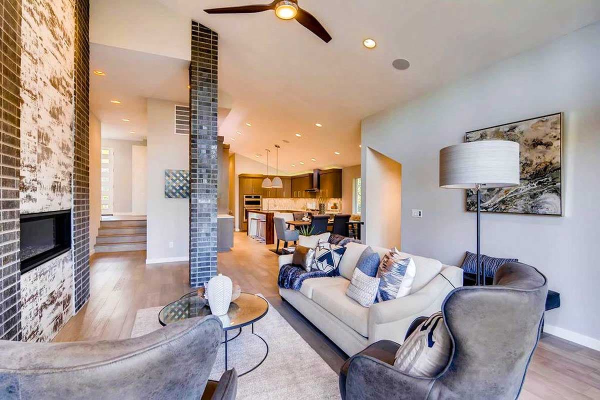 Interior view of open-concept living space with vaulted ceiling, brick fireplace, and kitchen visible.