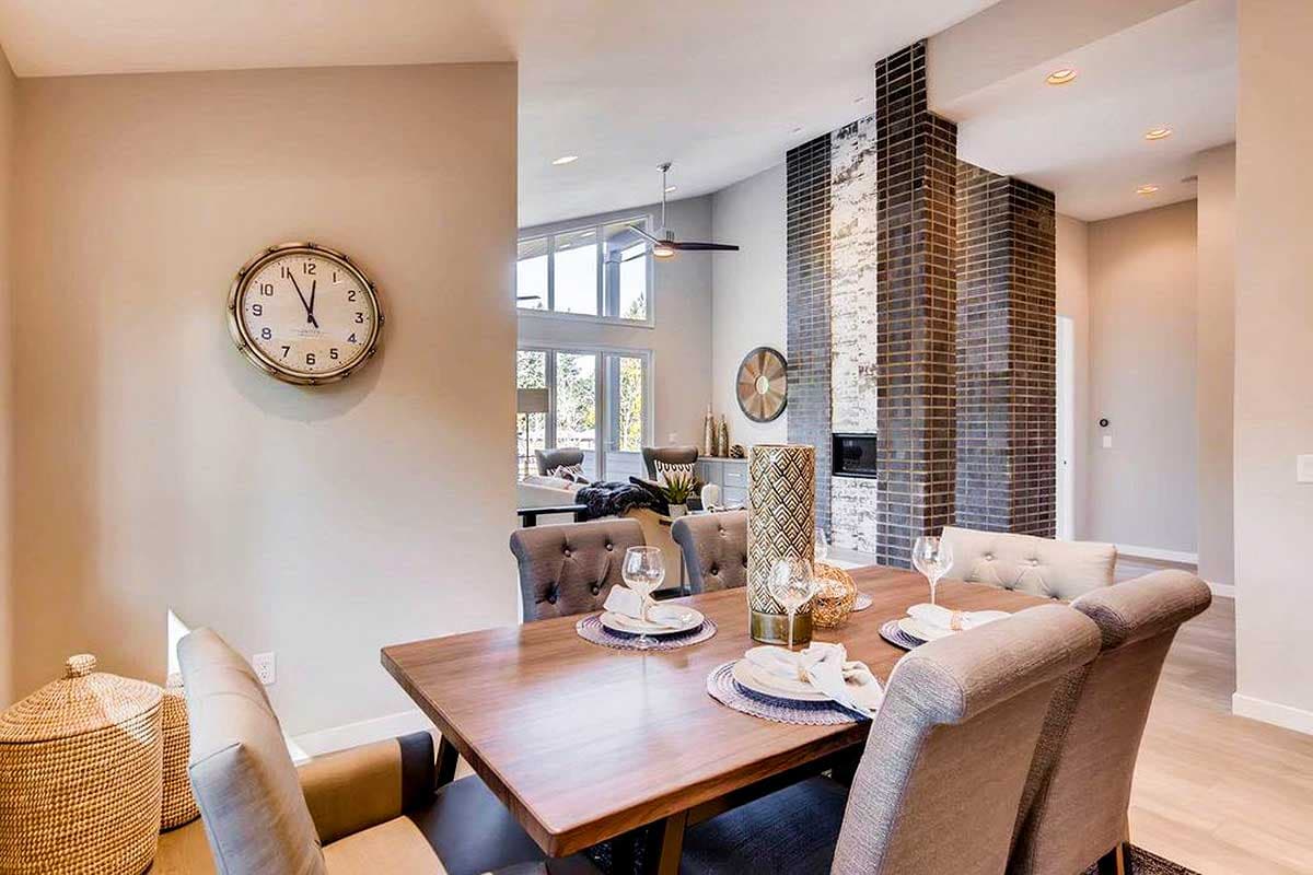 Dining area with tufted chairs and a wooden table, adjacent to a living area with a large brick fireplace and vaulted ceiling.