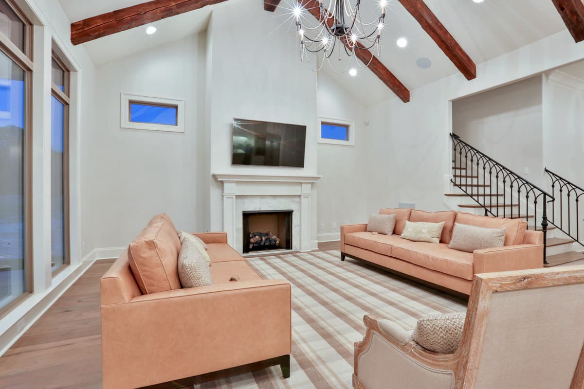 Interior view of living room with exposed beams, fireplace, large windows, and staircase.