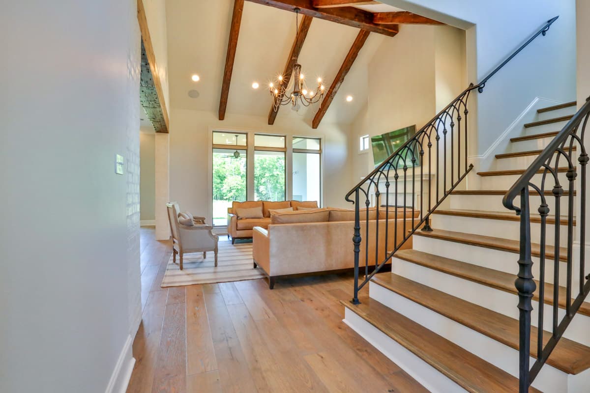 Interior view of living room with vaulted ceiling, exposed beams, ornate chandelier, and wrought iron staircase.