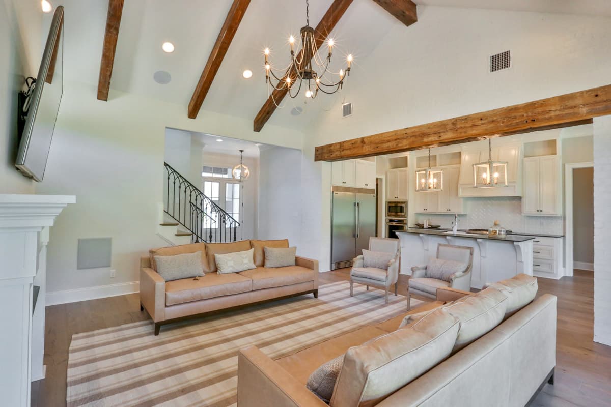 Great room with vaulted ceiling, exposed beams, fireplace, and open kitchen with island and white cabinetry.