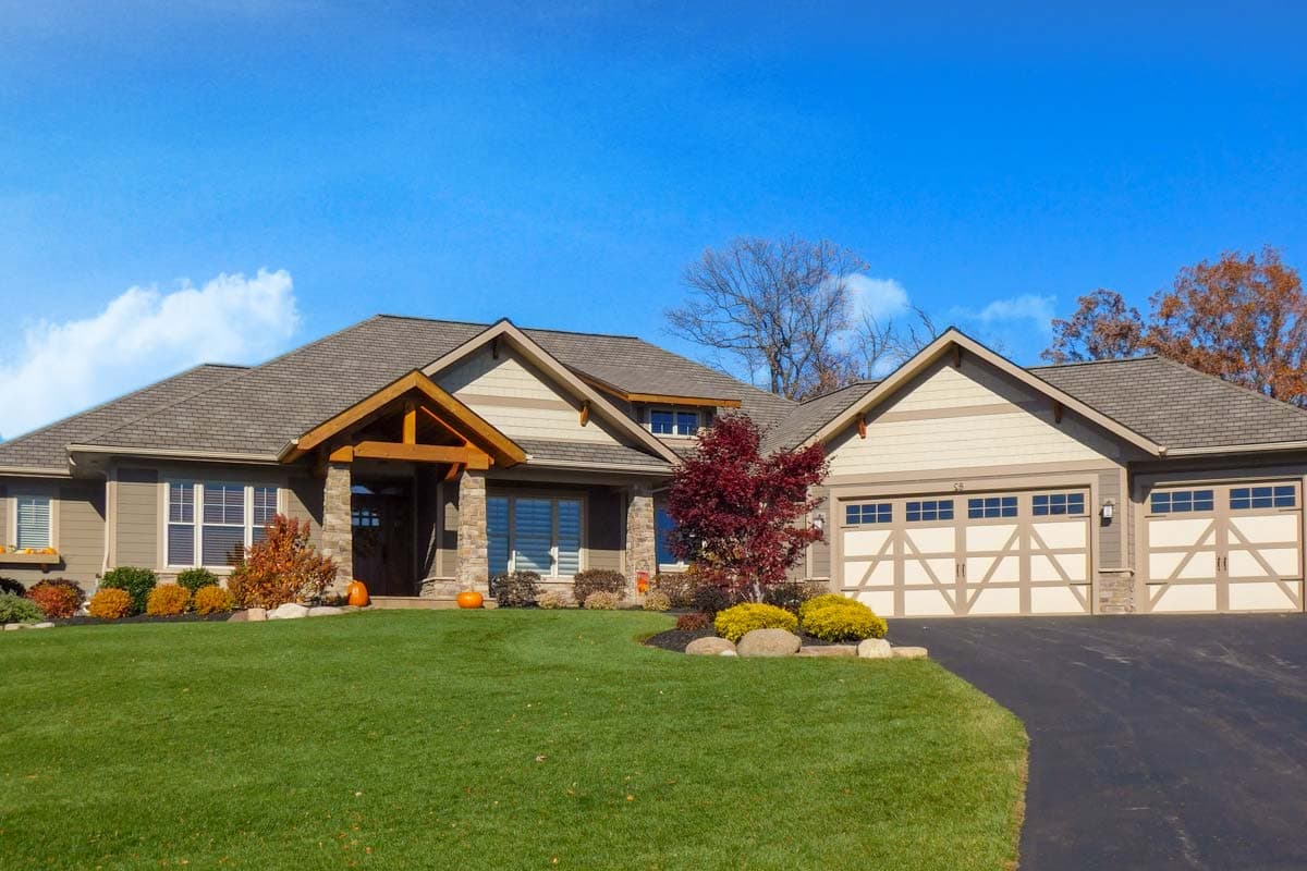 House plan exterior: Ranch style, stone and vinyl siding, covered entryway, and a three-car garage with decorative doors.