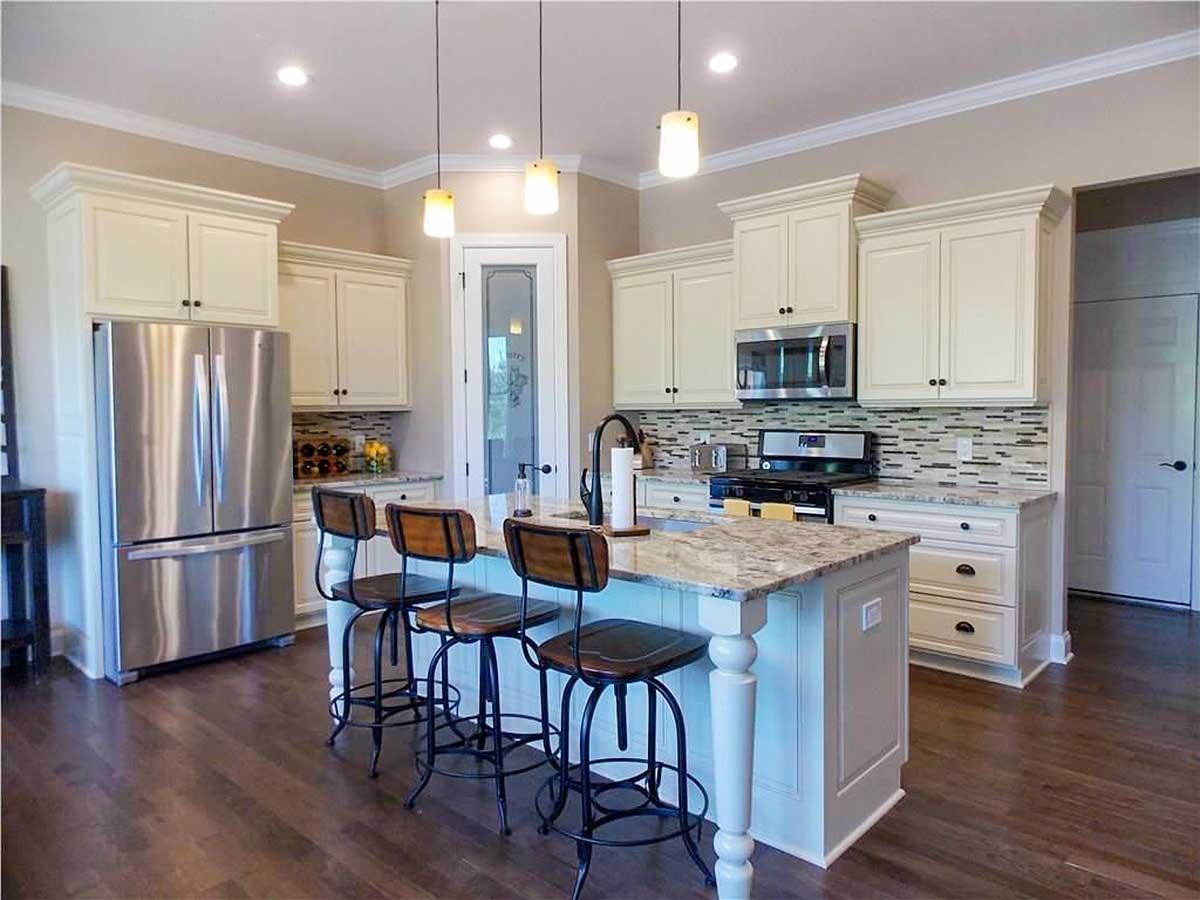 Kitchen with island, stainless steel refrigerator, range, and pendant lights.