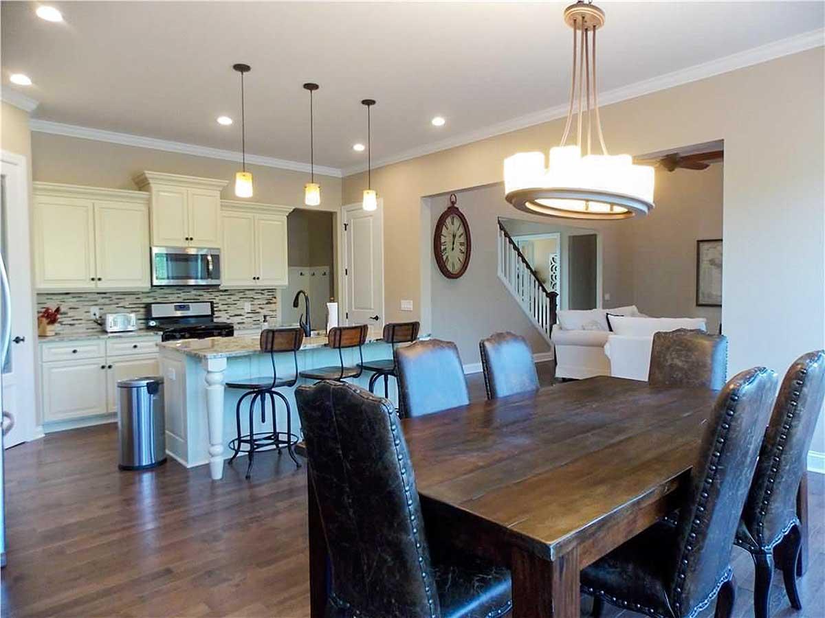 Kitchen and dining area with island, pendant lights, wooden table, leather chairs, and stairs leading to upper level.