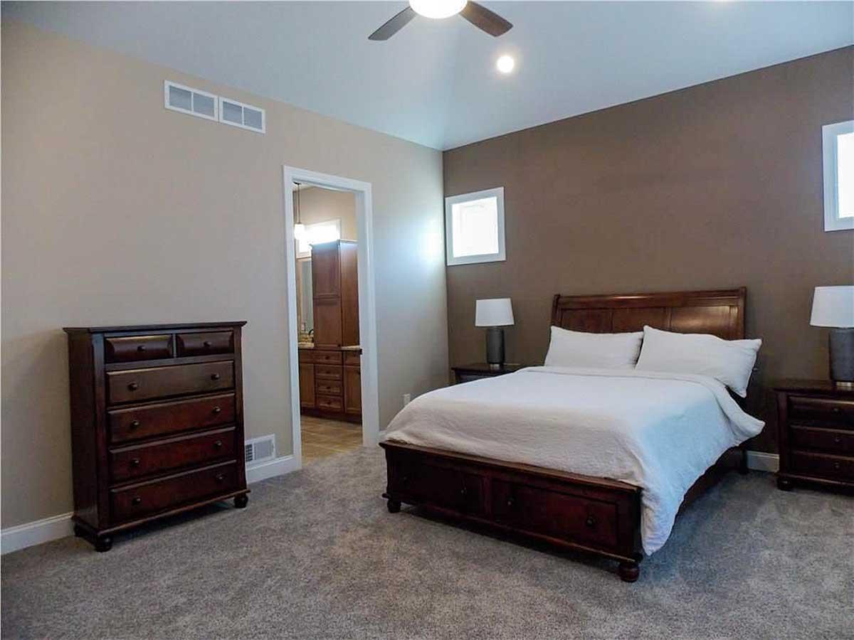 Bedroom with king bed, wooden dresser, and doorway to ensuite bathroom with double vanity and wood cabinets.