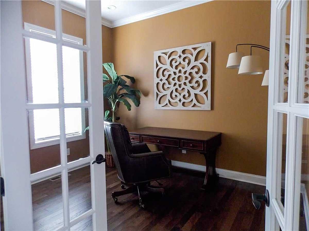 Office interior with French doors, desk, leather chair, and decorative wall art.