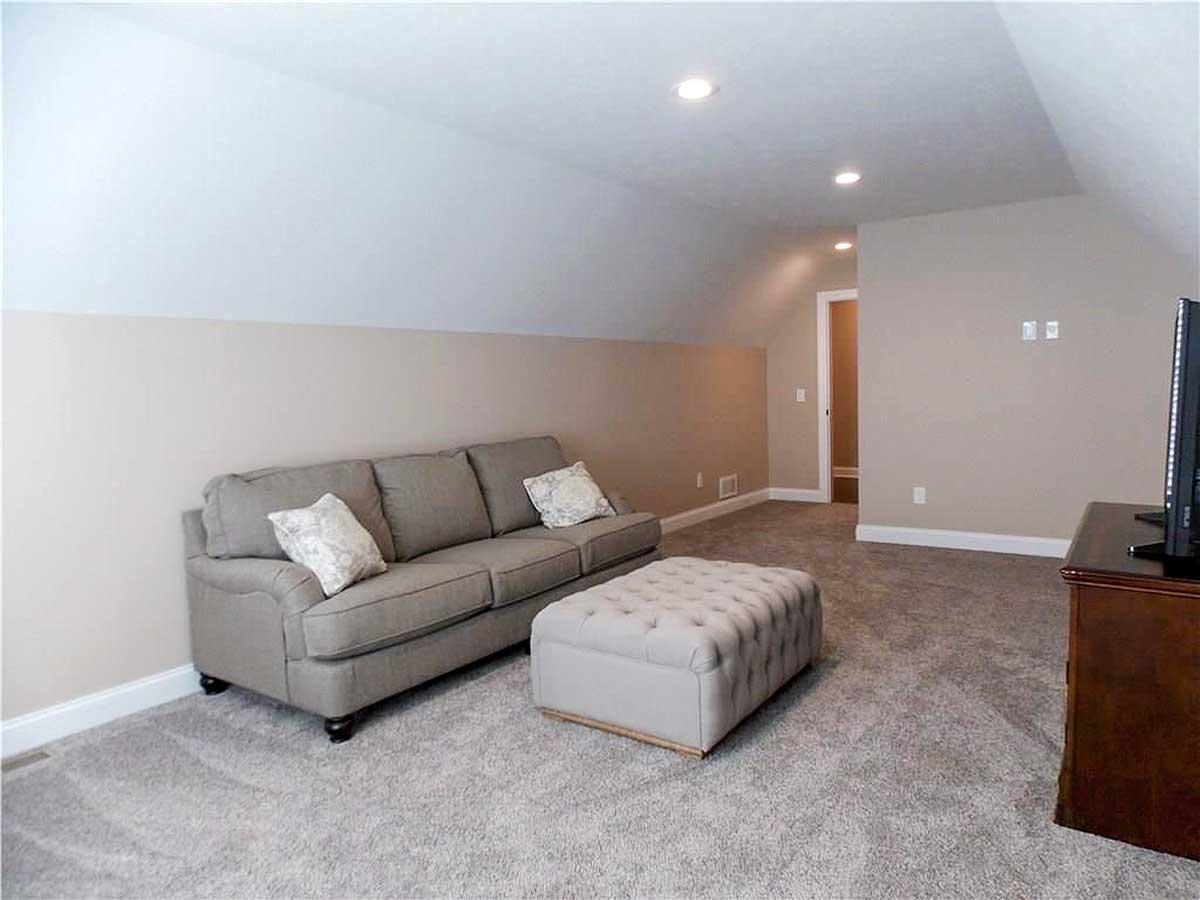 Interior view of a finished attic room with a gray sofa, tufted ottoman, and sloped ceilings.