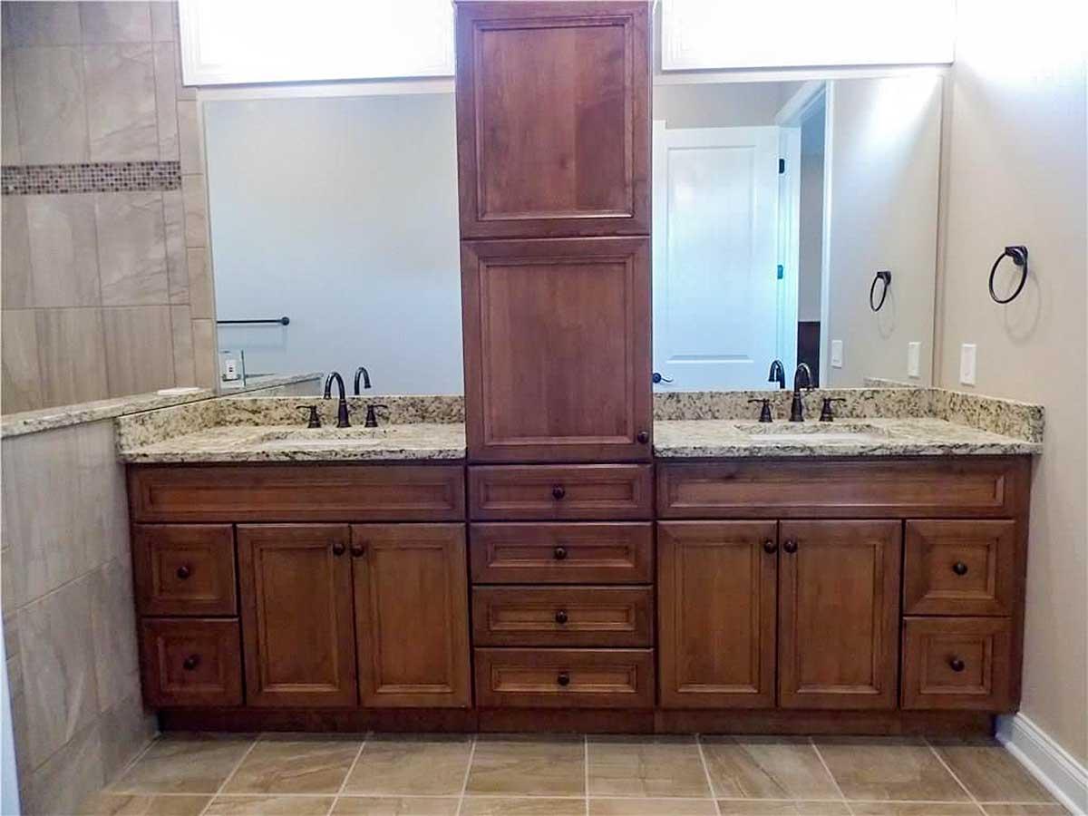 Bathroom vanity with double sinks, granite countertops, wooden cabinetry, and a tall central cabinet.