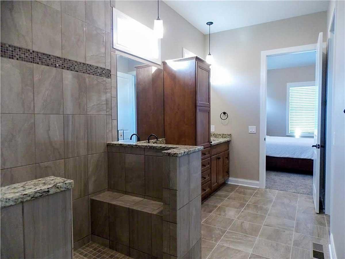 Bathroom with tiled walk-in shower, double vanity with wood cabinets, and adjoining bedroom.