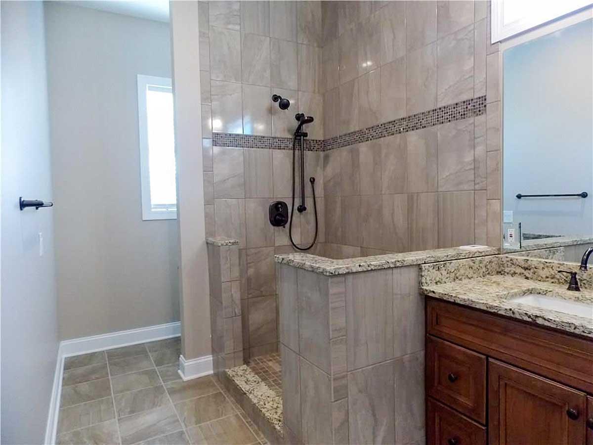 Tiled walk-in shower with granite accents and a modern vanity with a granite countertop.