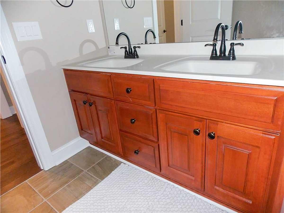Bathroom vanity with double sinks, cherry cabinets, dark hardware, and a white countertop.