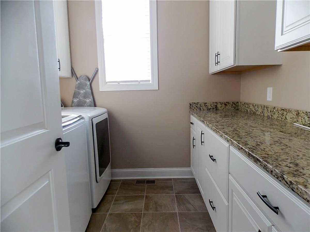 Laundry room with white cabinets, granite countertop, washer, dryer, and ironing board.