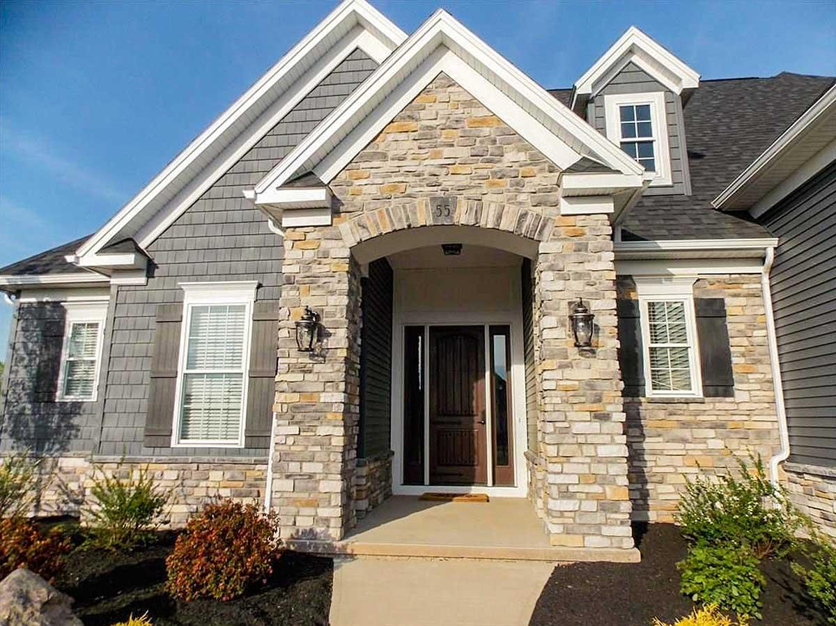 House plan exterior with stone facade, arched entryway, shingle siding, gabled rooflines, and dormer.