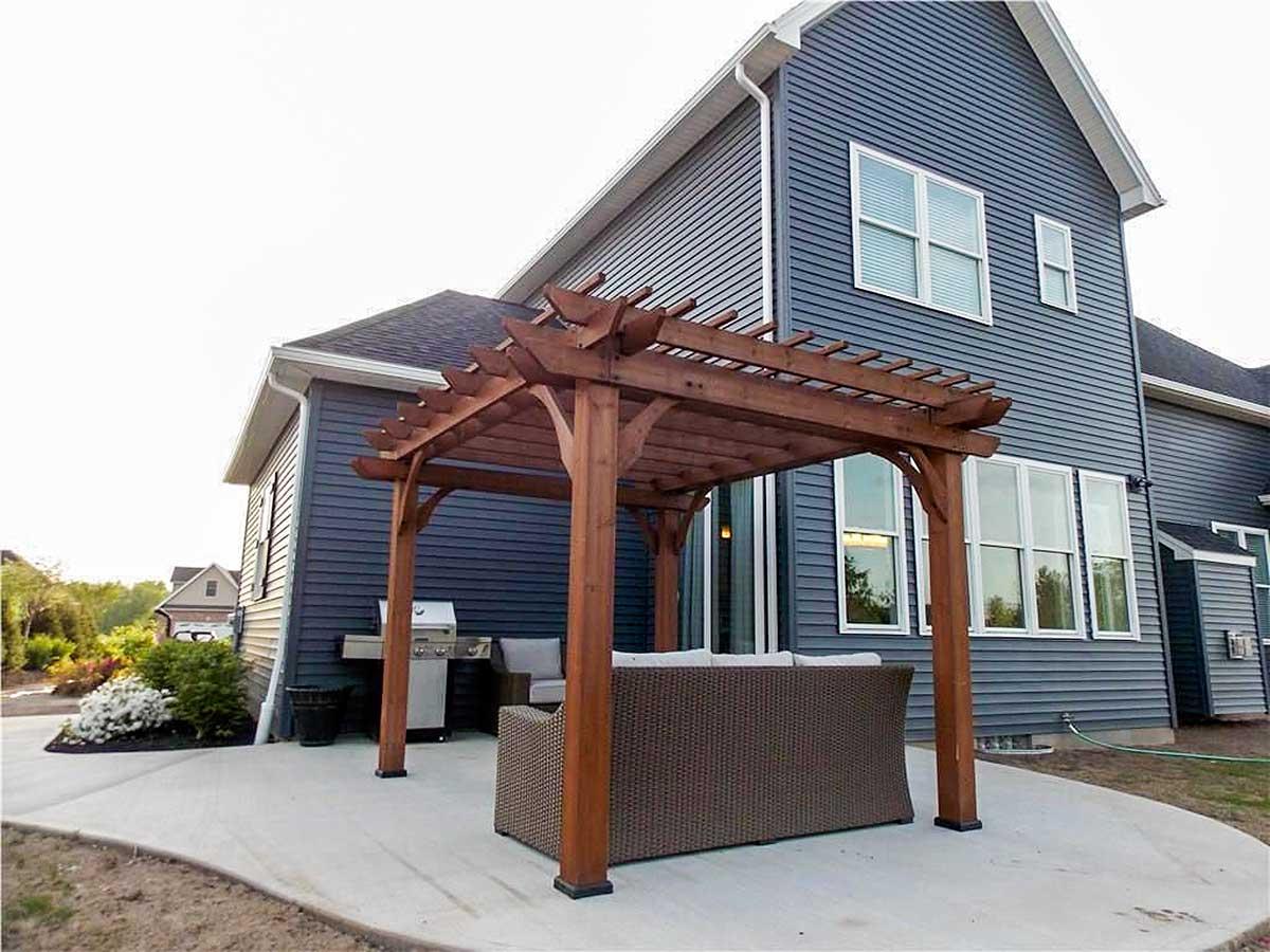 House plan exterior features dark blue siding, white-trimmed windows, and a wooden pergola over a patio with outdoor furniture.