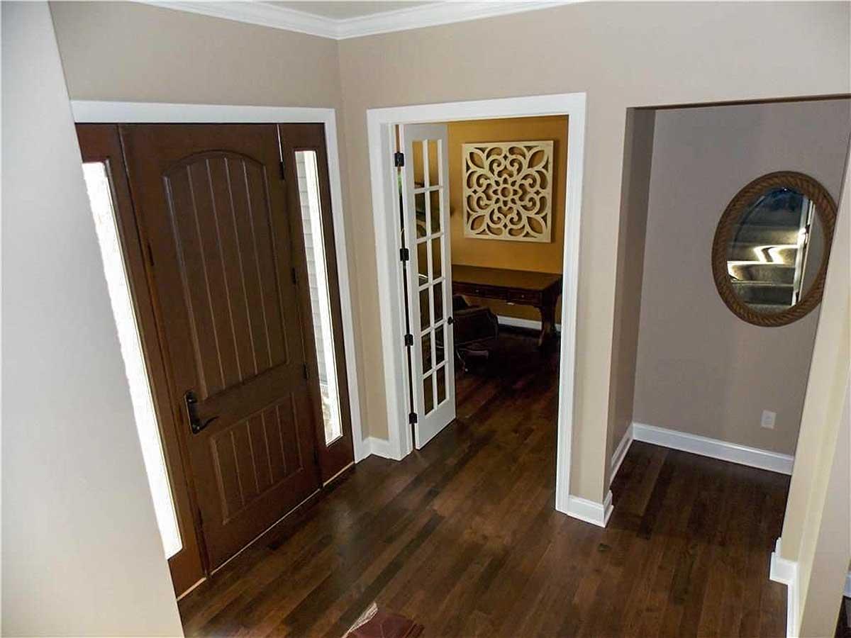 Interior view of entryway with dark wood door, glass sidelights, and doorway to office with French doors.