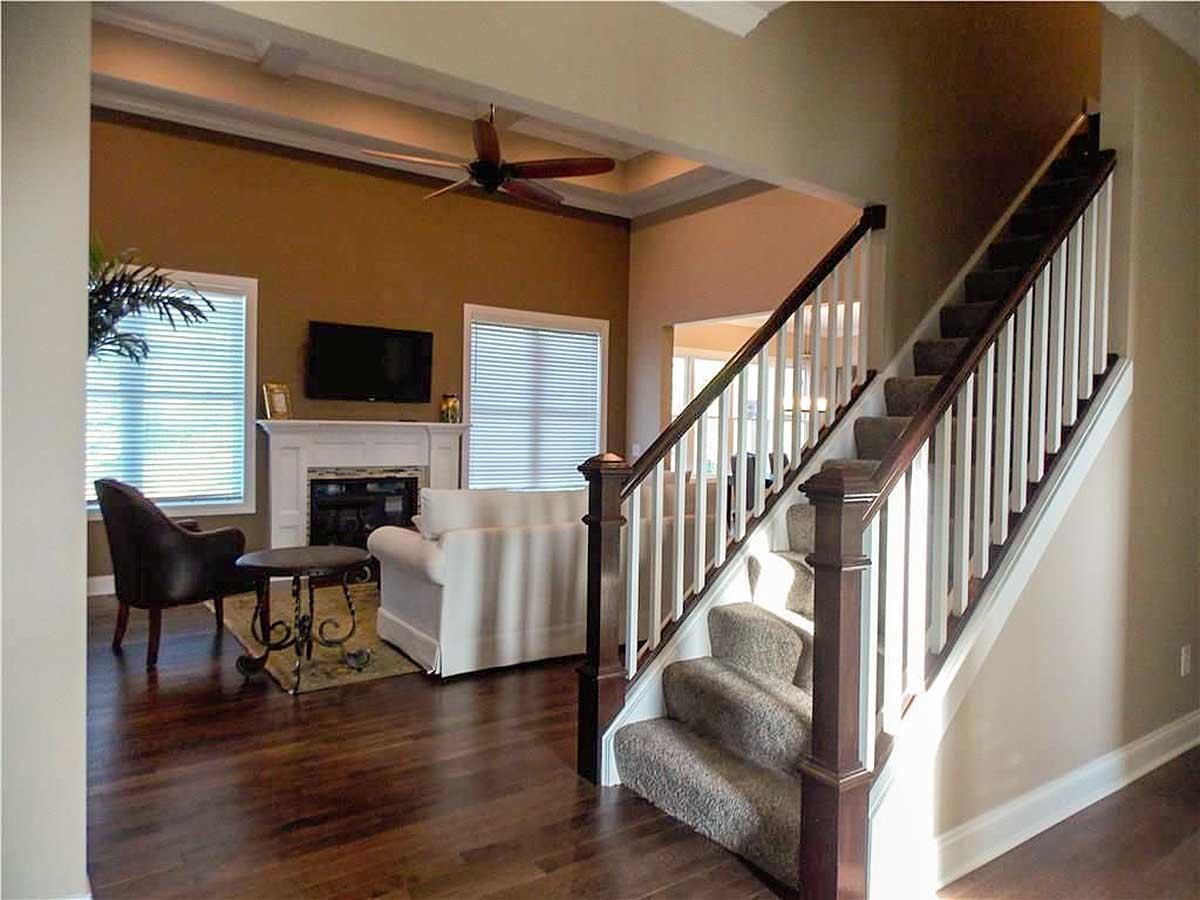 Living area with fireplace and media center, adjacent to staircase with white balusters and dark wood railings.