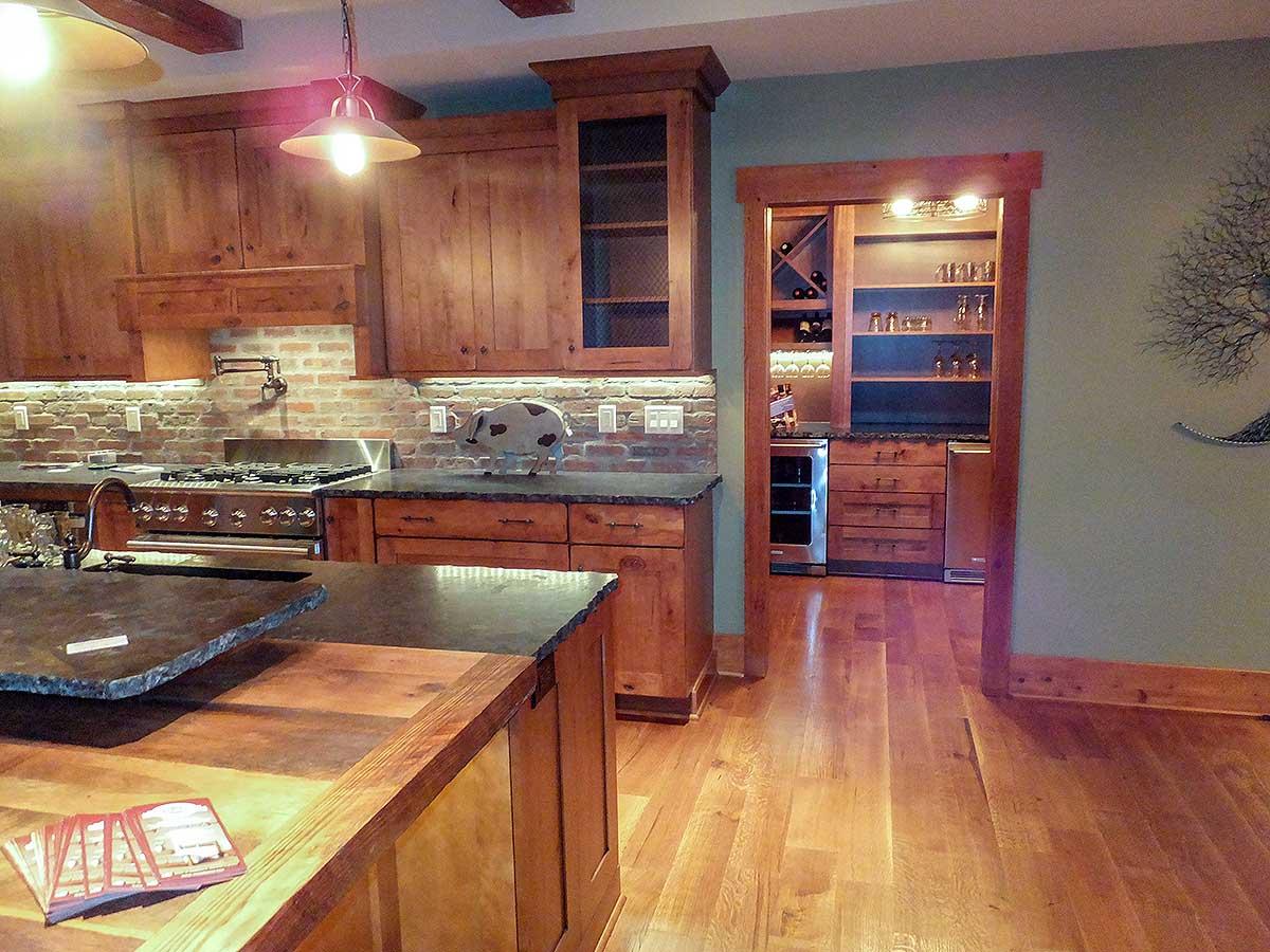 Kitchen with exposed brick backsplash, wood cabinetry, and a built-in wine and beverage bar with mini-fridges.