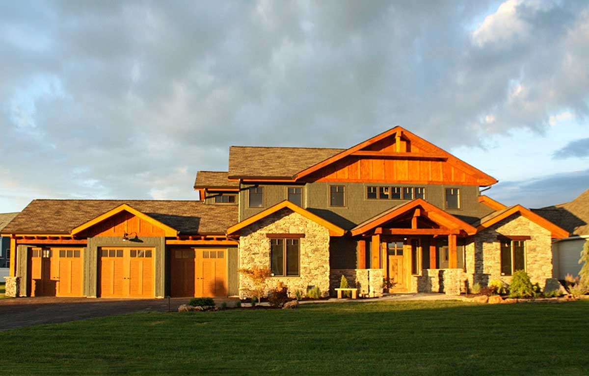 House plan exterior in Craftsman style. Two-story home with gabled rooflines, exposed timber porch supports, and a three-car garage.