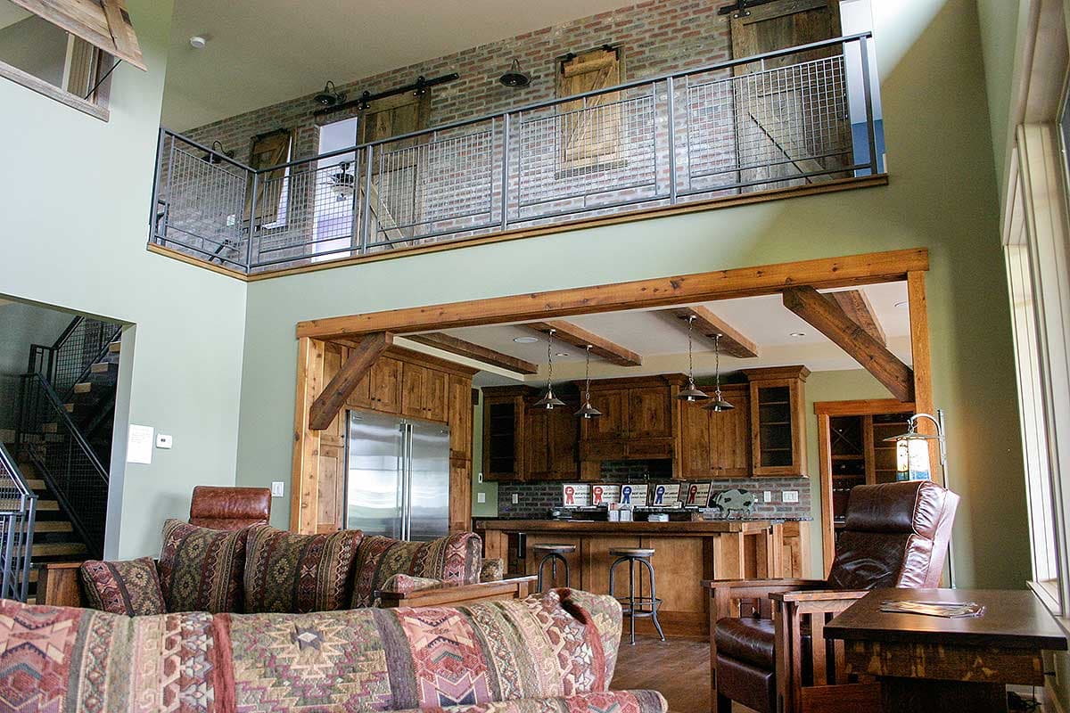 Interior view of living area with exposed beams, loft railing, brick accent wall with barn doors, and kitchen.