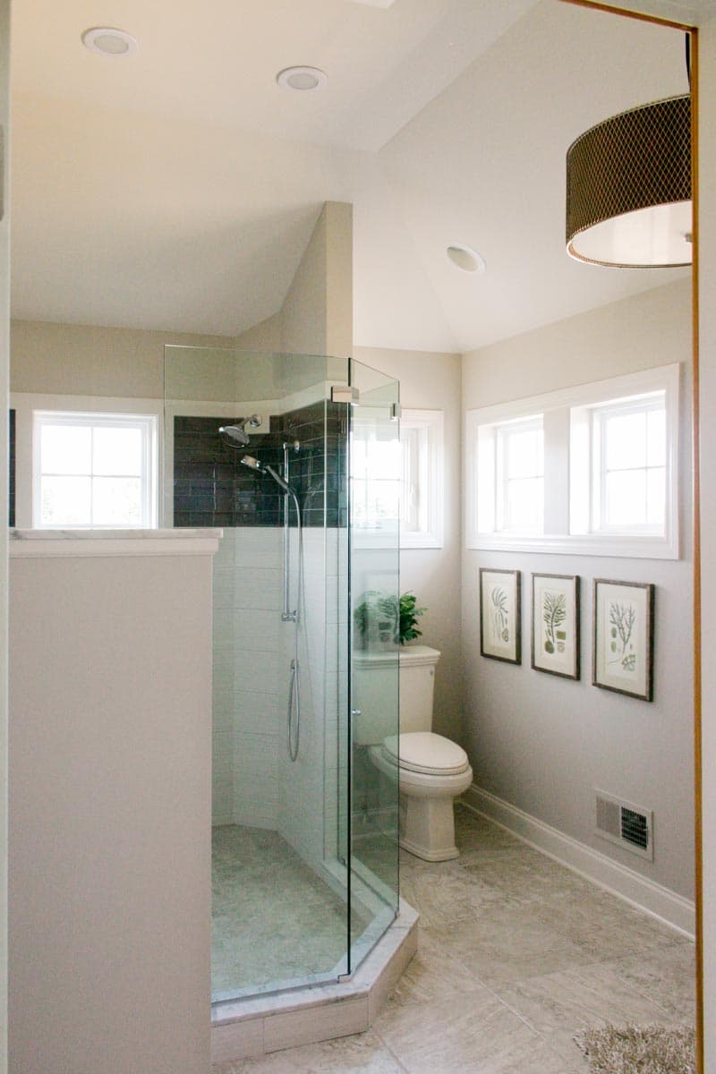 Bathroom with glass-enclosed shower, toilet, and three framed botanical prints on wall.