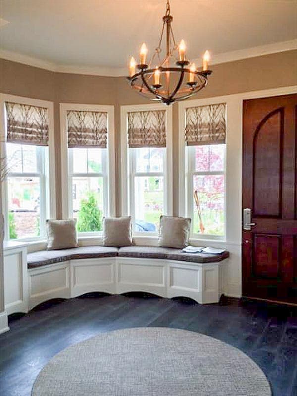 Interior view of a sunroom with bay windows, built-in seating, and a rustic chandelier.