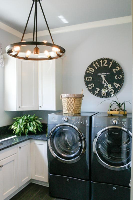 Laundry room with white cabinets, granite countertops, washer and dryer set, decorative clock, and circular chandelier.