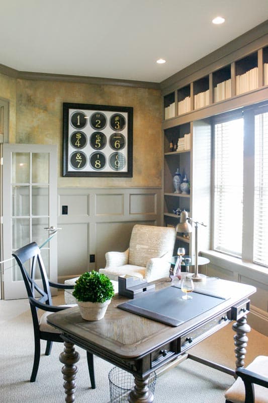 Home office with desk, patterned armchair, glass-paned door, and built-in shelving with books.