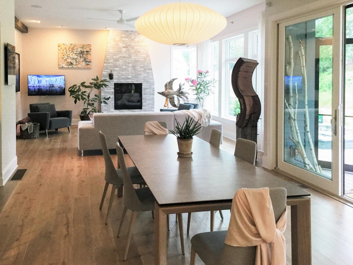 Dining area with stone fireplace and large windows; view to sliding glass doors with birch branches.