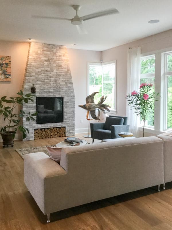 Interior view of a living room featuring a floor-to-ceiling stacked stone fireplace, sectional sofa, and large windows.