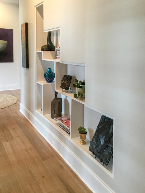 Interior hallway with recessed shelving unit displaying decorative objects and artwork on wall.