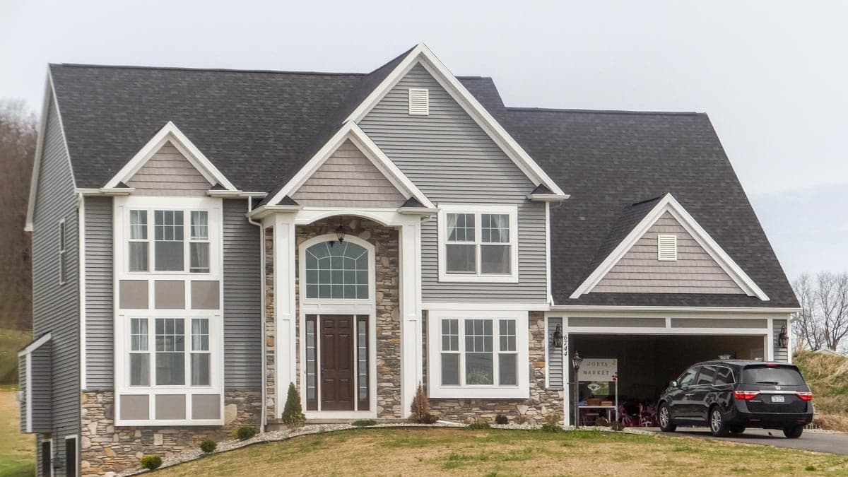 House plan exterior. Two-story home with gables, stone facade, and a two-car garage. Features a covered entry and multiple dormers.
