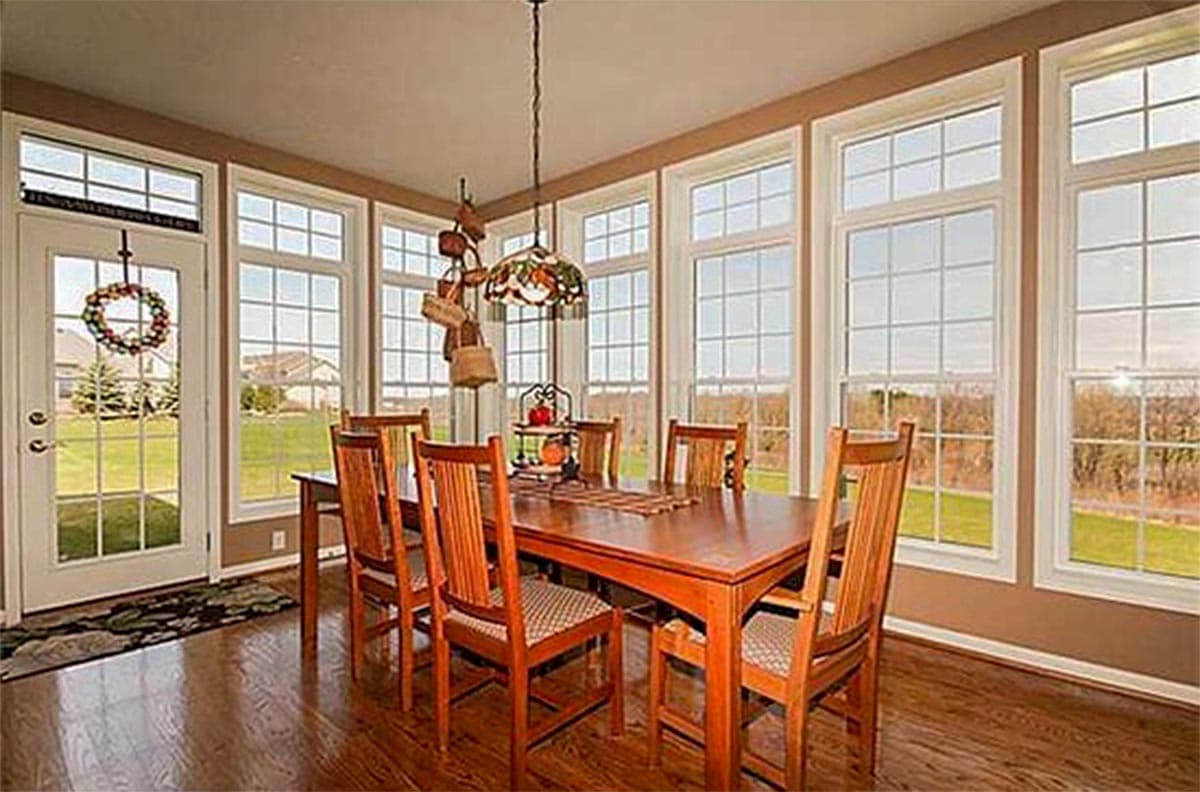 Dining room with wood table, chairs, and wall of windows overlooking a grassy yard.