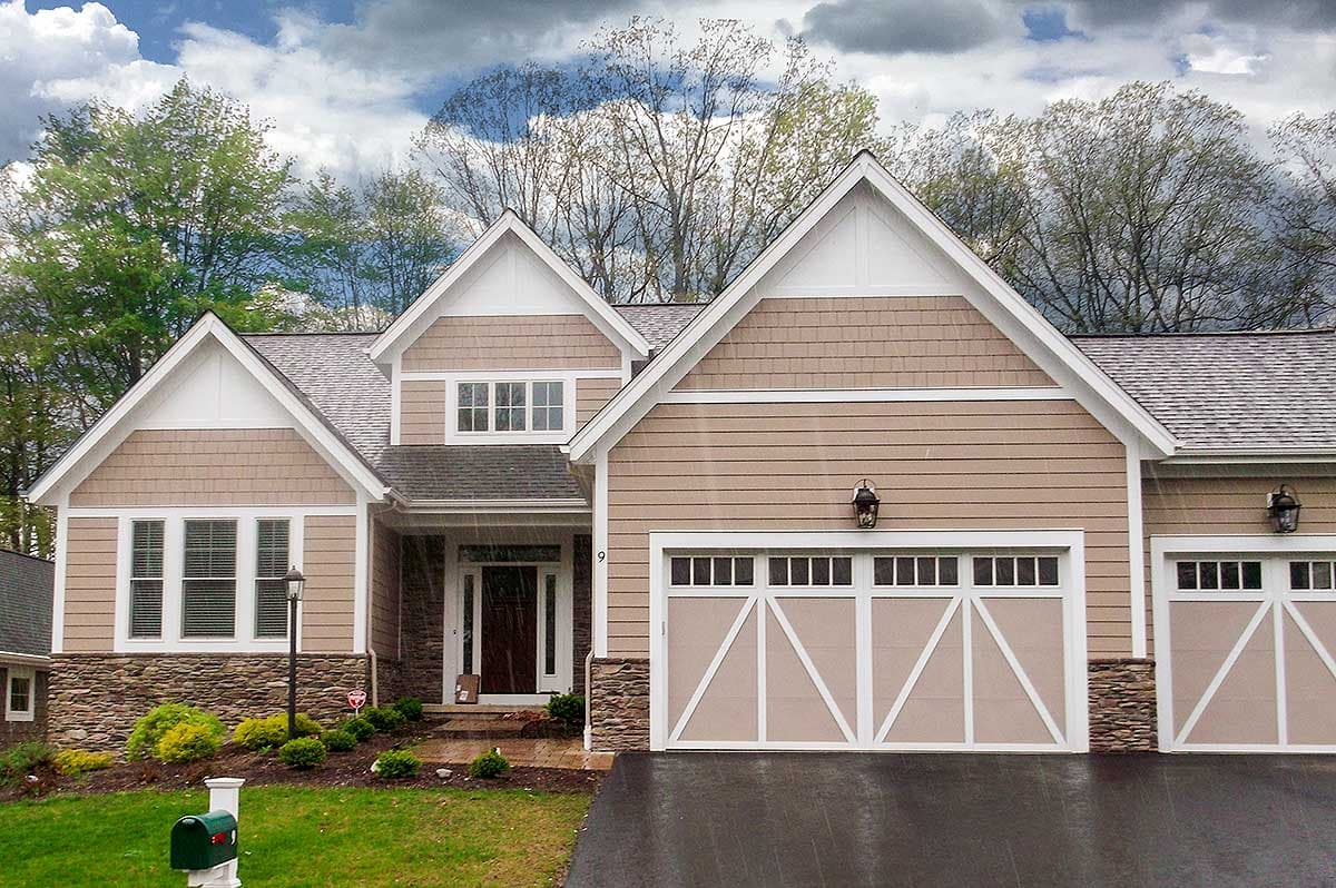 House plan exterior: Two-story home with stacked stone foundation, horizontal siding, gables, and a side-facing two-car garage.