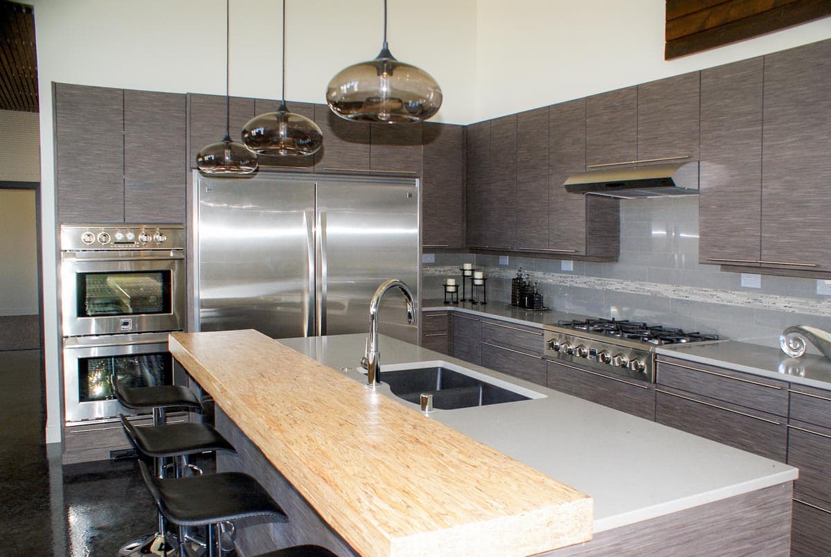 Modern kitchen with stainless steel appliances, gray cabinetry, waterfall island with seating, and pendant lighting.