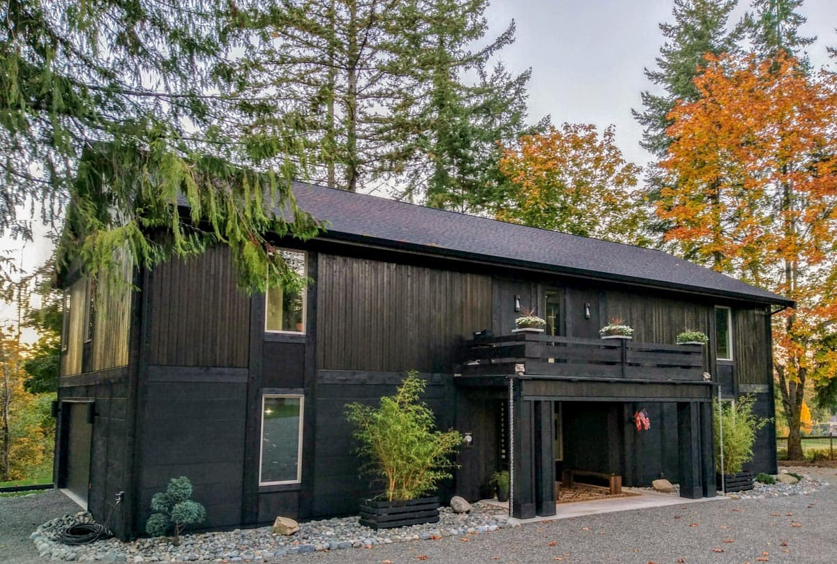 Modern house plan exterior with dark vertical siding, second-story balcony, and covered entryway.