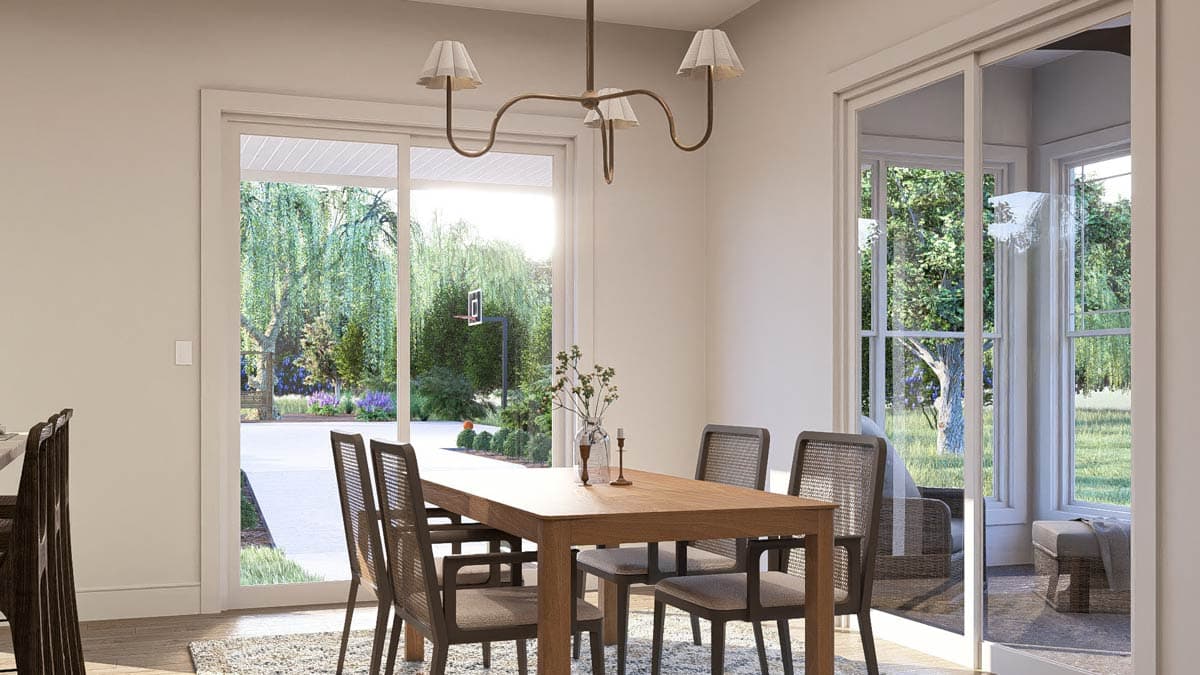 Dining room with wooden table and chairs, featuring large sliding glass doors and windows overlooking a backyard with trees.